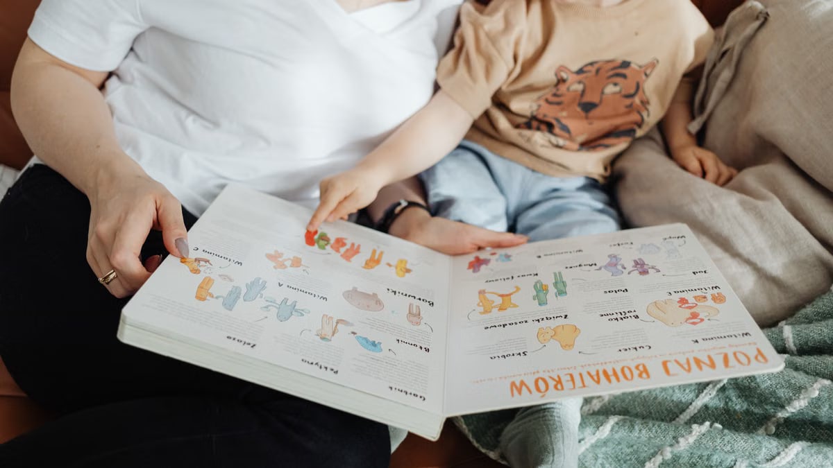 A mother and her son enjoy reading a children's book together while sitting on a cozy couch.