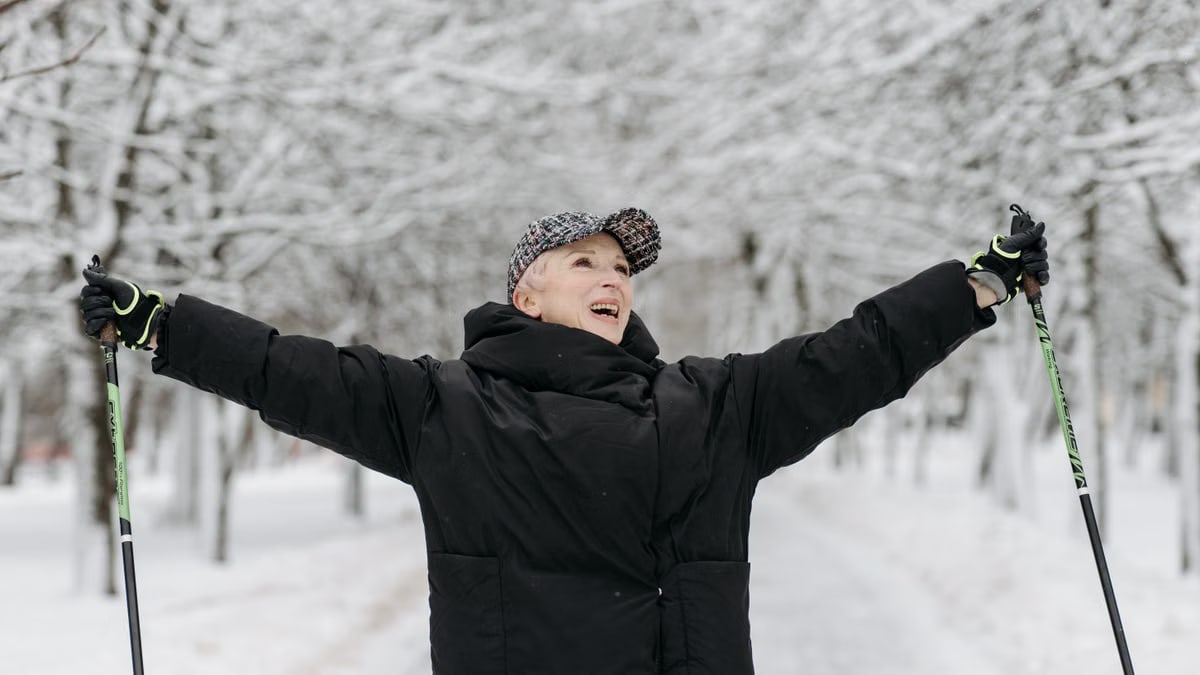 Senior woman celebrates with raised arms while skiing in a snowy park, exuding joy and freedom.